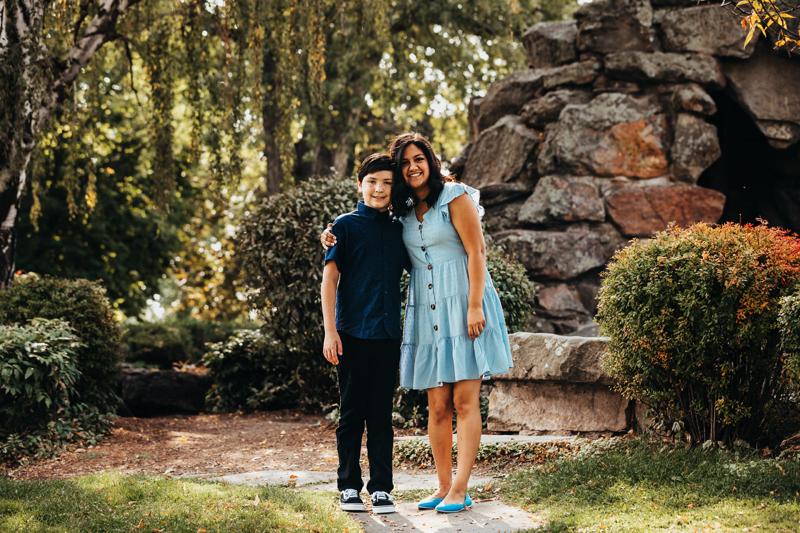 Brother and sister hugging standing on a path in green foiliage