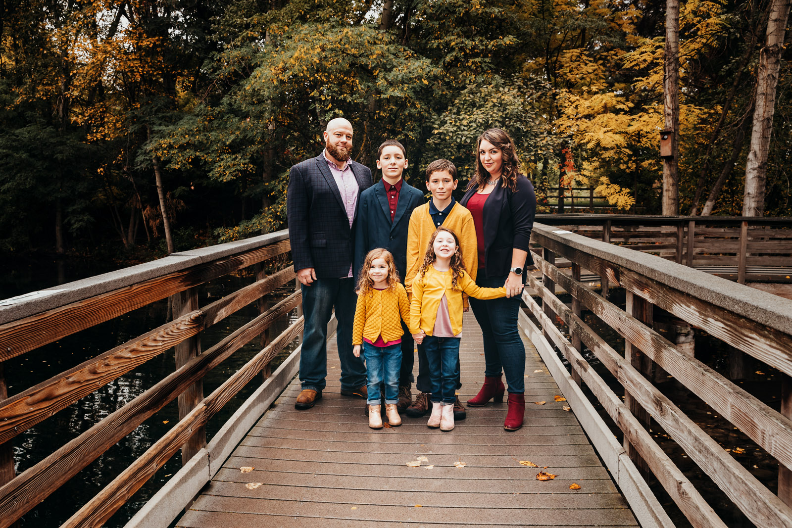 Family of six standing on a bridge holding hands and smiling.  two brothers and two sisters