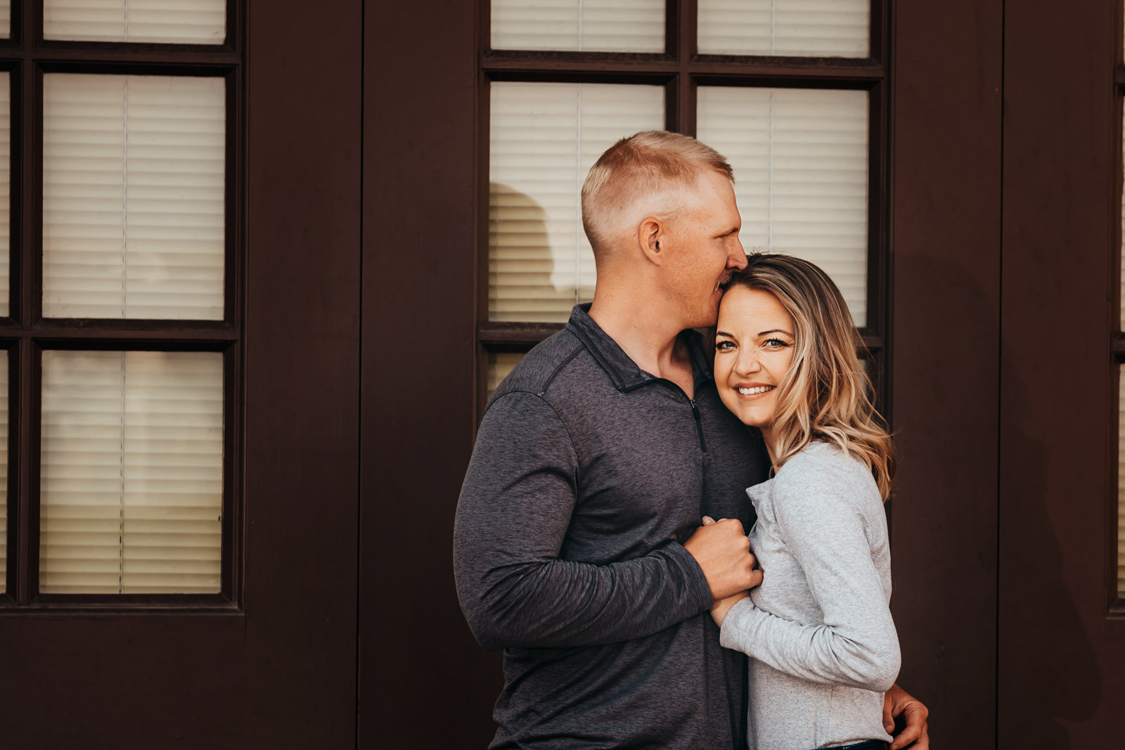husband and wife standing in front of door hugging and husband kissing wife on top of head