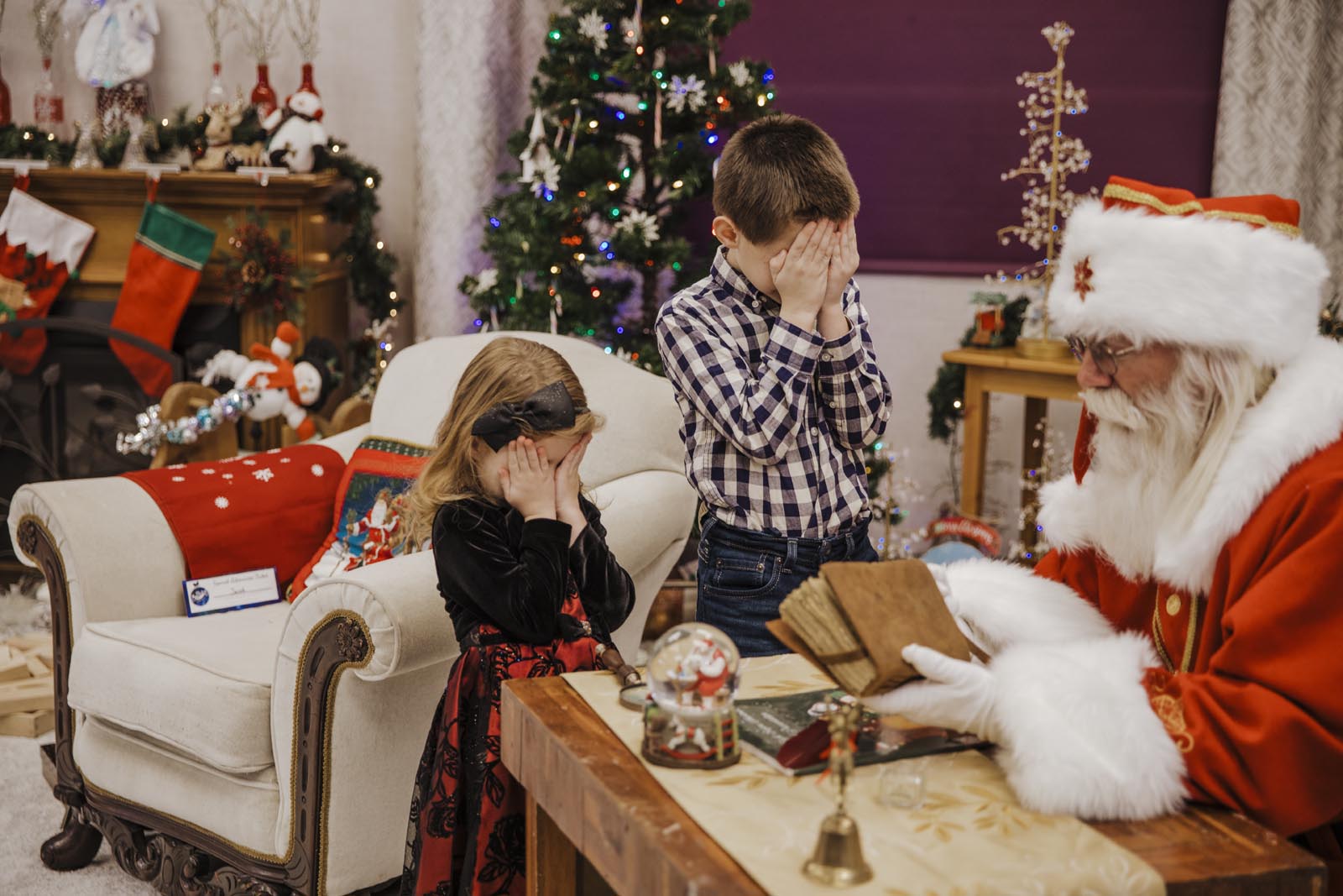 Boise Santa Pictures brother and sister hiding their eyes while Santa is about to surprise them at his desk