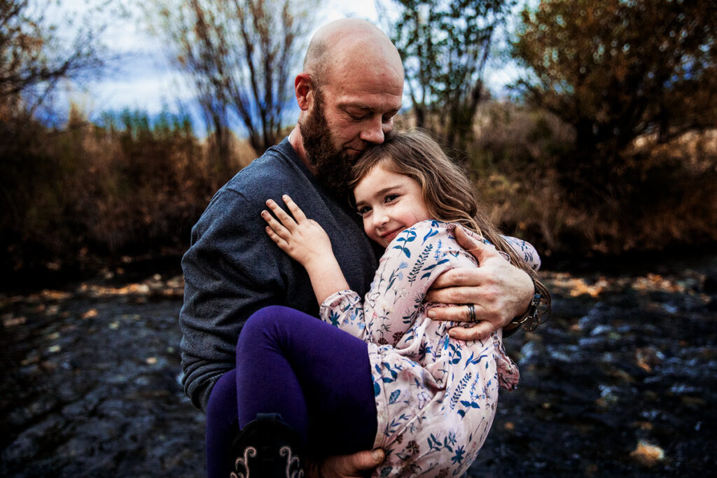 bald dad hugging his daughter and looking down at her smiling