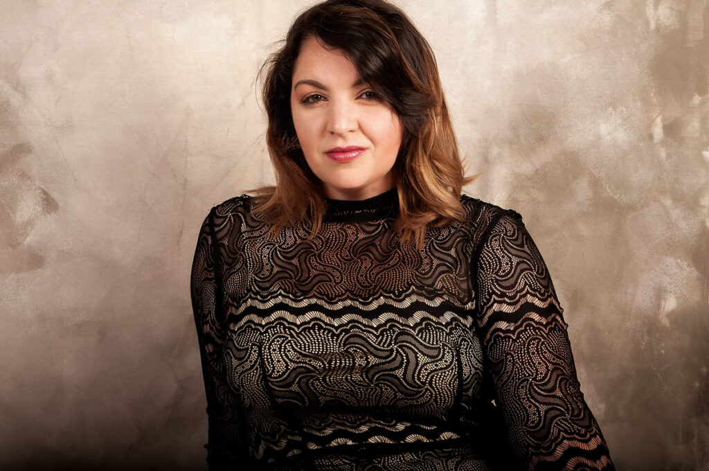 brunette with blond highlights wearing black lace top smiling
