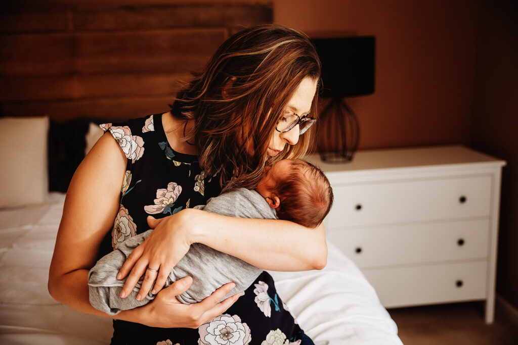 mom with glasses holding baby newborn kissing him on forehead
