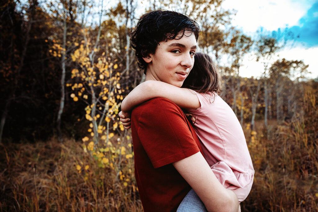 big brother with dark hair and red shirt holding baby sister