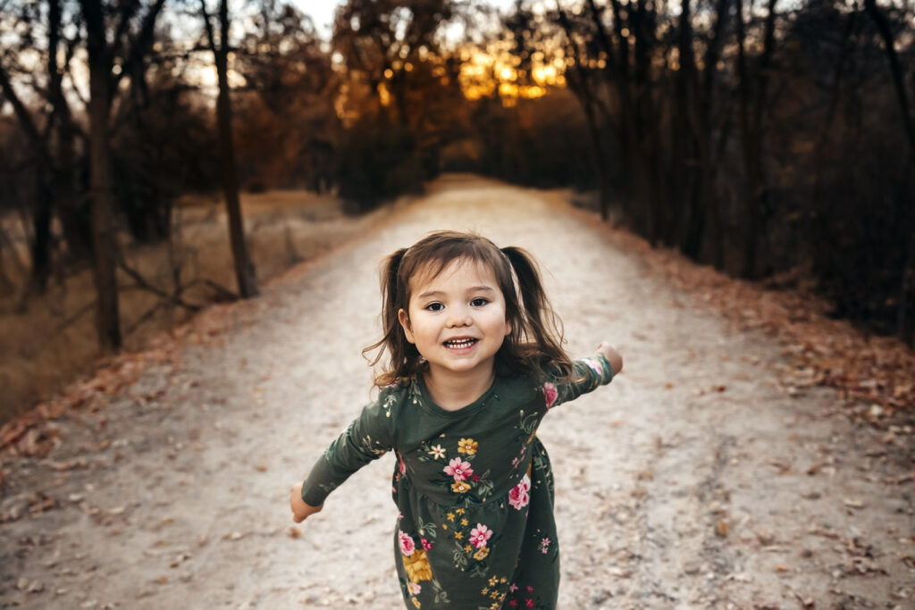 adorable little girl with pigtails and green dress smiling standing on a trail