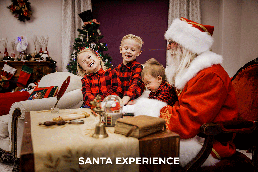 three kids with santa laughing hysterically while he is sitting at his desk showing them a book and holding baby sister