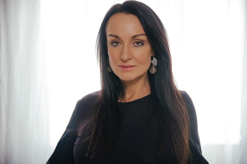 brunette with long dark hair wearing black top backlit