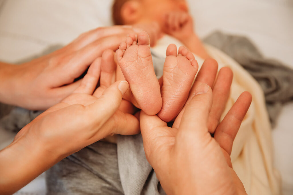 mom and dad holding newborn's feet in their hands while he sleeps