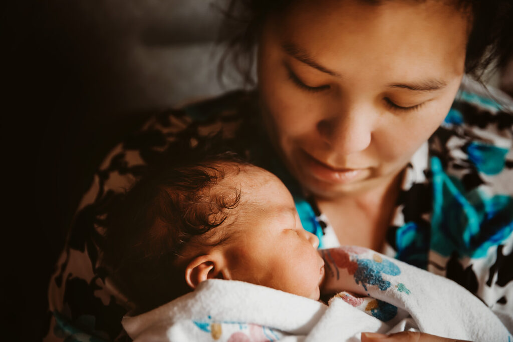 mom in floral top holding newborn baby boy looking down at him