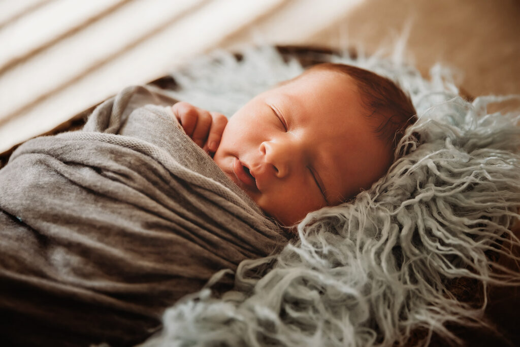 newborn baby boy swaddled in gray sleeping in basket with blue flokati
