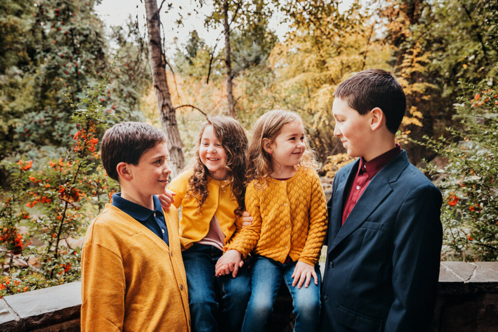 two brothers and two sisters sitting near a wall smiling at each other wearing blues and yellows